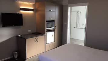 A hotel room with a bed, a kitchenette with a microwave, a TV, and a shower area.