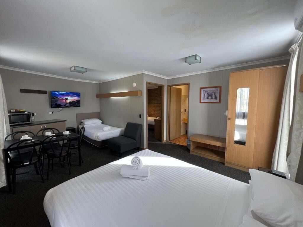 A hotel room with a bed, a desk with chairs, a television, and a bathroom visible through an open door.