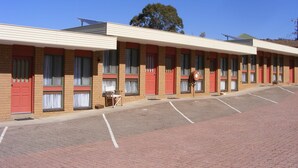Een motel met meerdere kamers, elk met een rode deur en een tafeltje buiten.