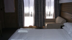 Een hotelkamer met een groot bed, een stoel en een raam met gordijnen.