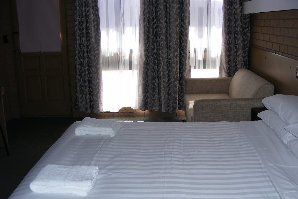Ett hotellrum med en stor säng, en stol och ett fönster med gardiner.