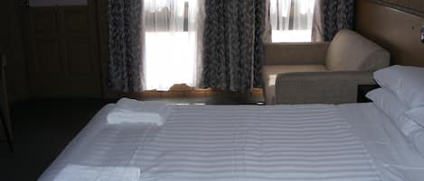 Una habitación de hotel con una cama grande, una silla y una ventana con cortinas.