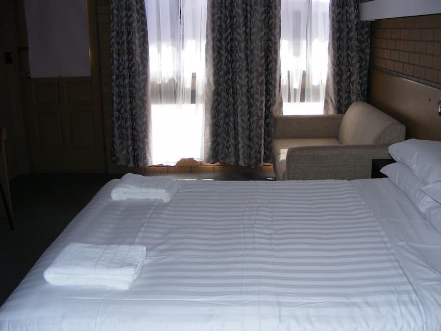A hotel room with a large bed, a chair, and a window with curtains.