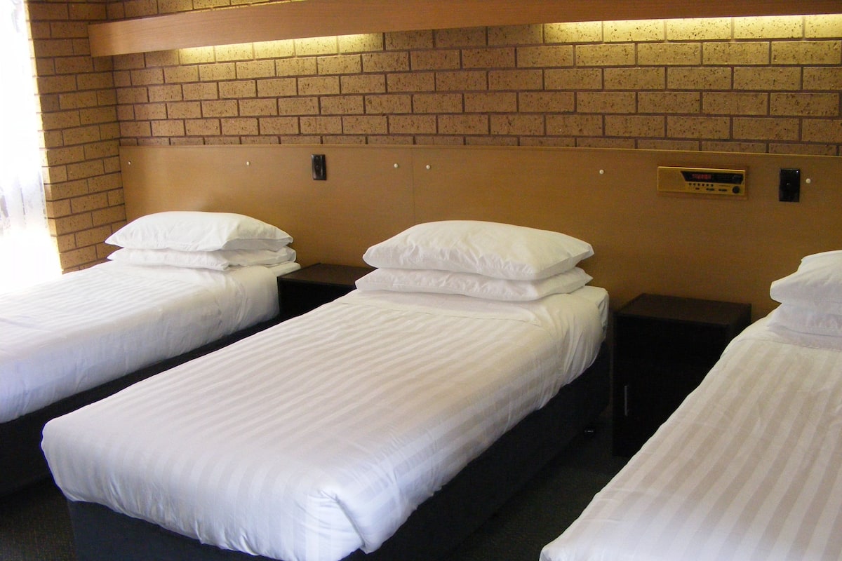 Ett hotellrum med tre separata sängar, alla med vita sängkläder och en mörk sänggavel.