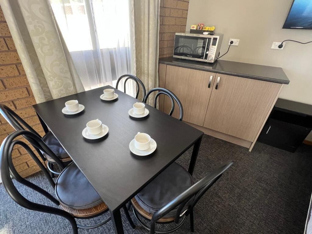 A dining area with a table set for four, four chairs, a microwave on a counter, and a TV mounted on the wall.