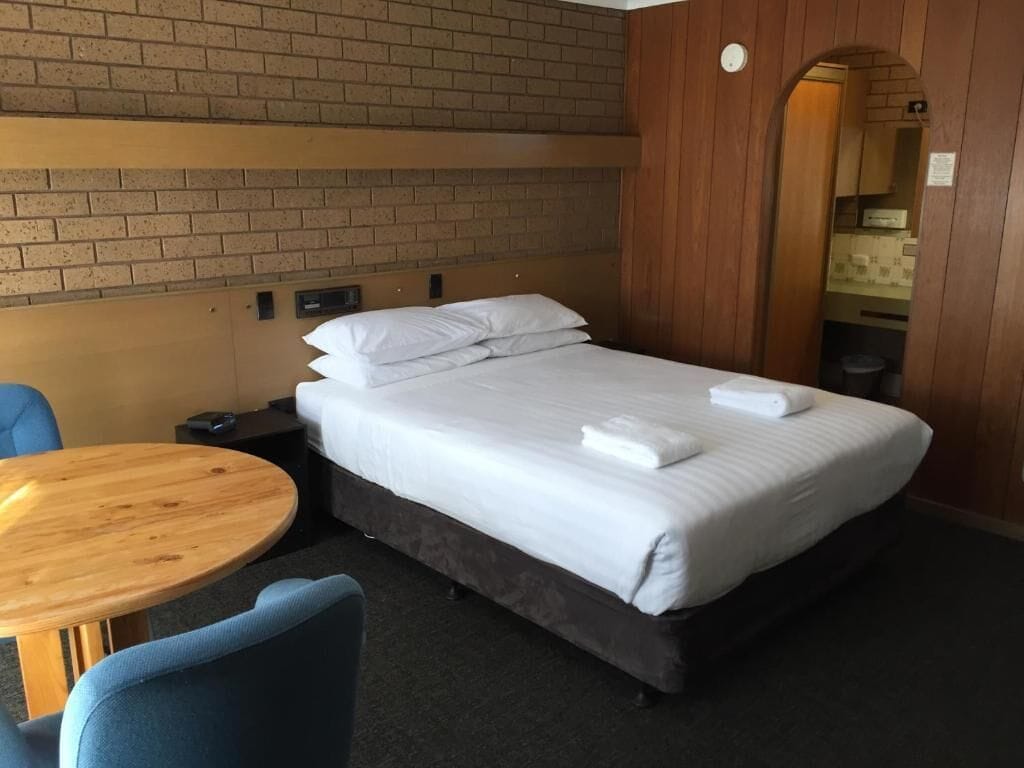 A hotel room with a single bed, a round wooden table, and a blue chair.