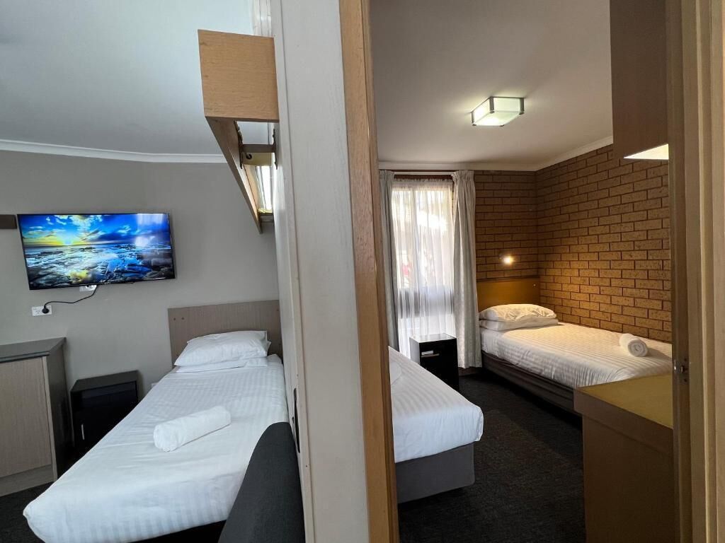 A hotel room with two beds, a television, and a brick wall.