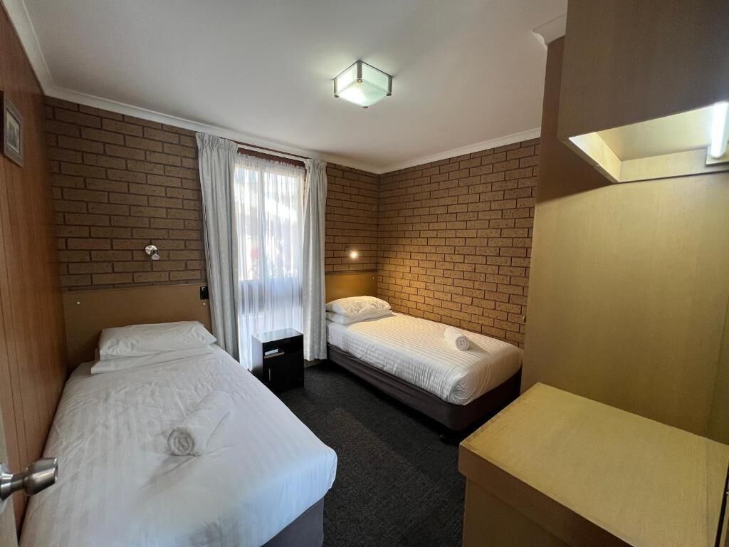 Une chambre d’hôtel avec deux lits, un petit bureau, un miroir et un mur décoré d’un motif en briques.