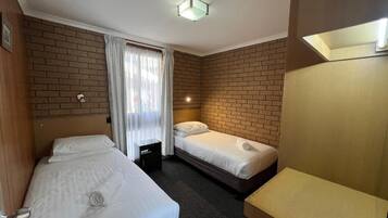 Une chambre d’hôtel avec deux lits, un petit bureau, un miroir et un mur décoré d’un motif en briques.