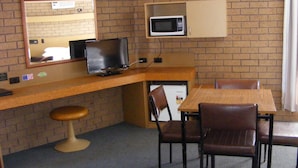 Een kleine kamer met een bakstenen muur, een televisie, een magnetron, een bureau en een stoel.