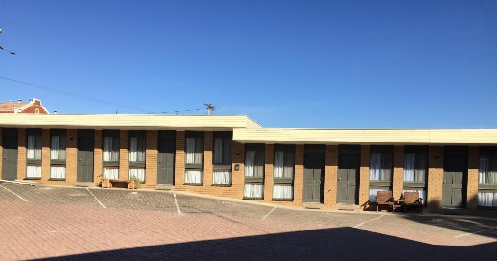 A motel with a row of rooms, a parking lot, and a clear blue sky.