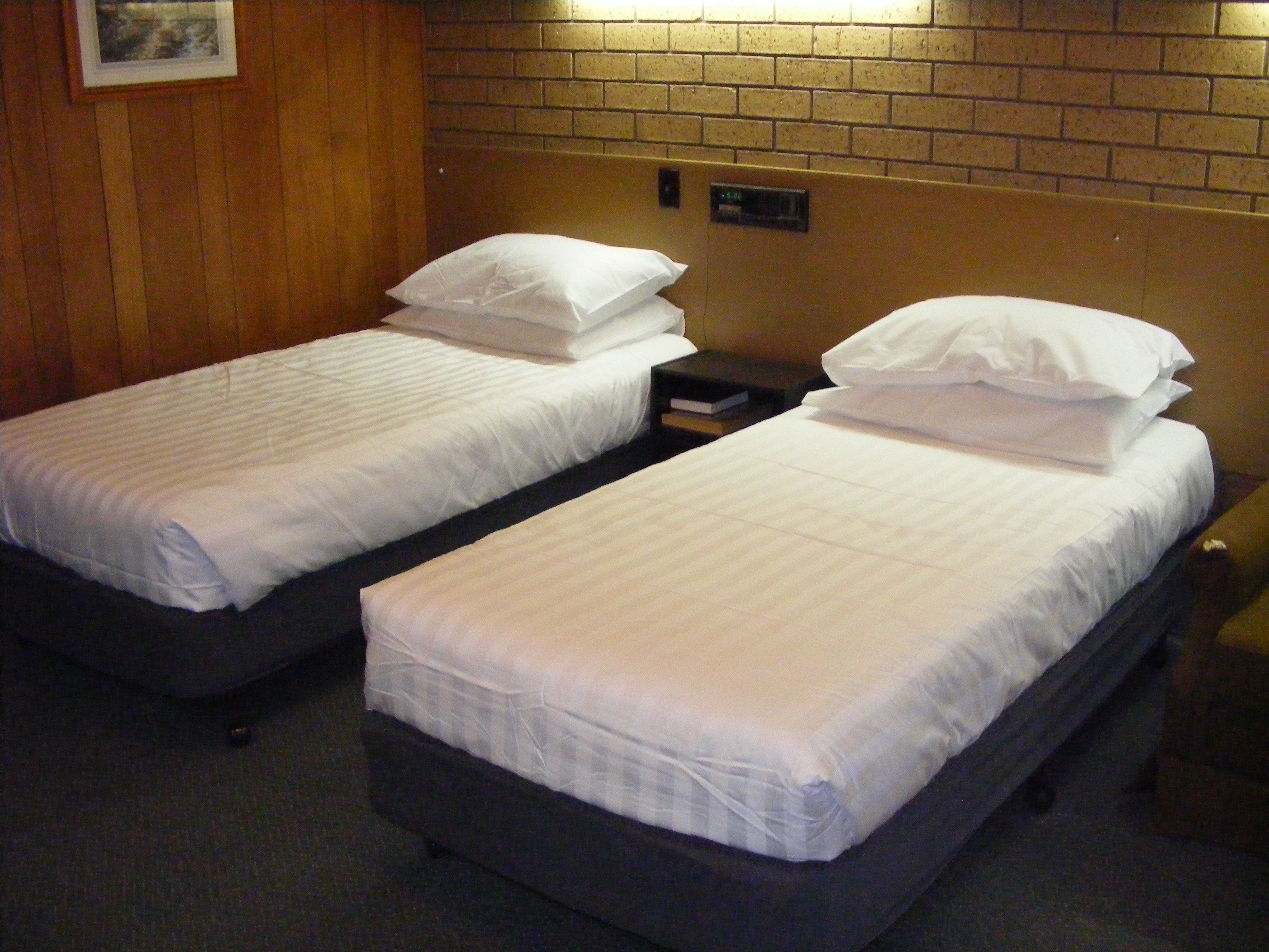 Two single beds with white linens, a wooden headboard, and a small nightstand with a book.