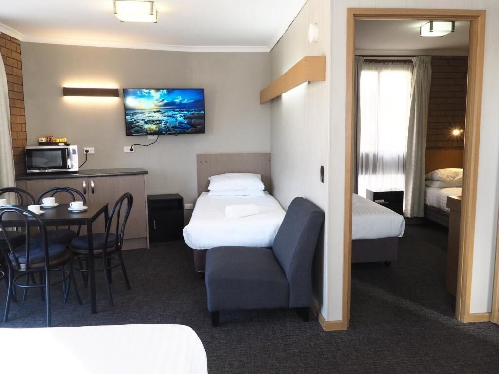 Habitación de hotel con cama, escritorio con microondas, televisión y zona de comedor con sillas.