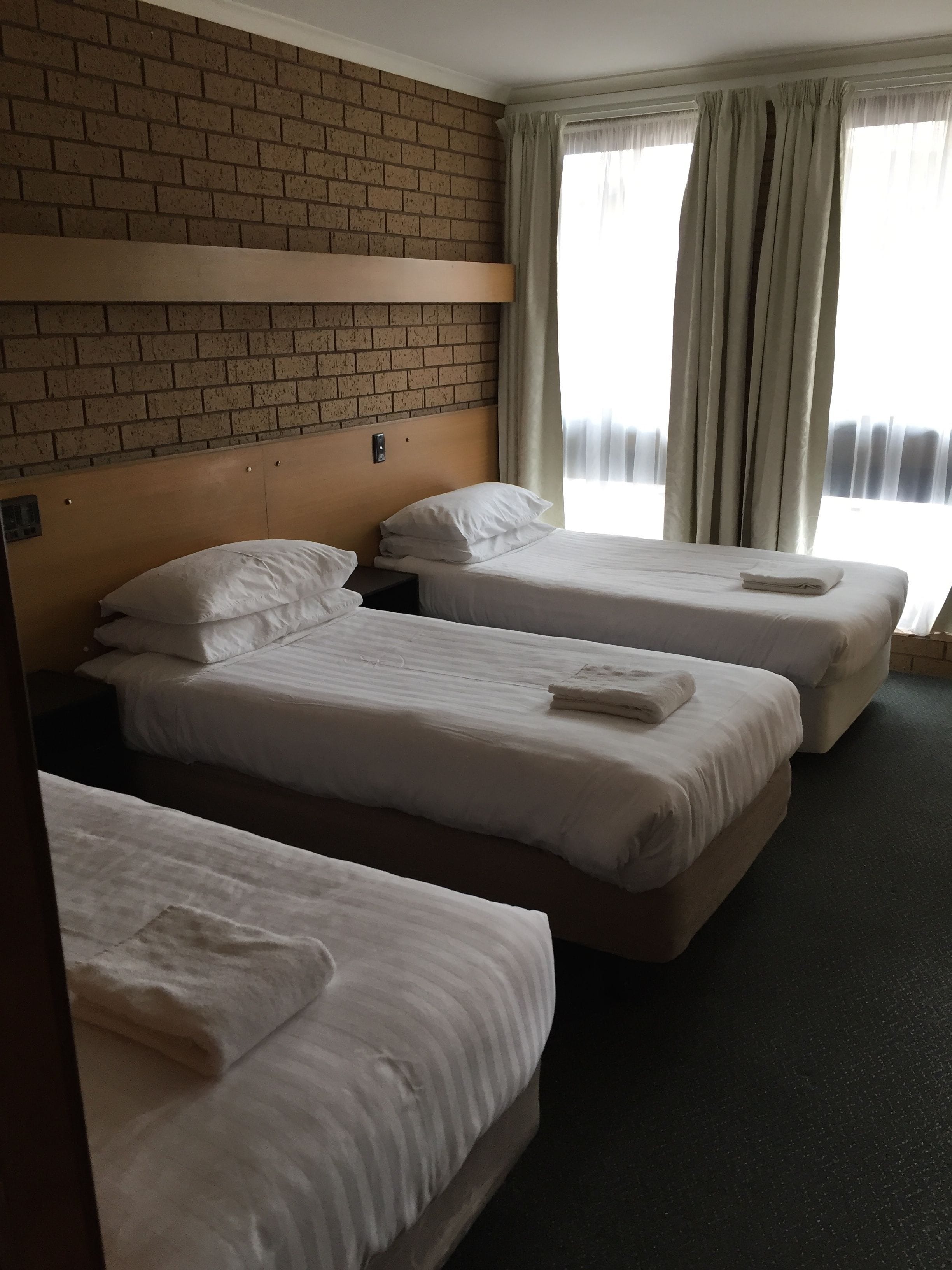 A hotel room with three single beds, a brick wall, and a window with curtains.
