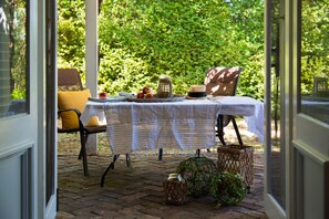 A patio with a table set for dining, surrounded by chairs and a wicker basket.