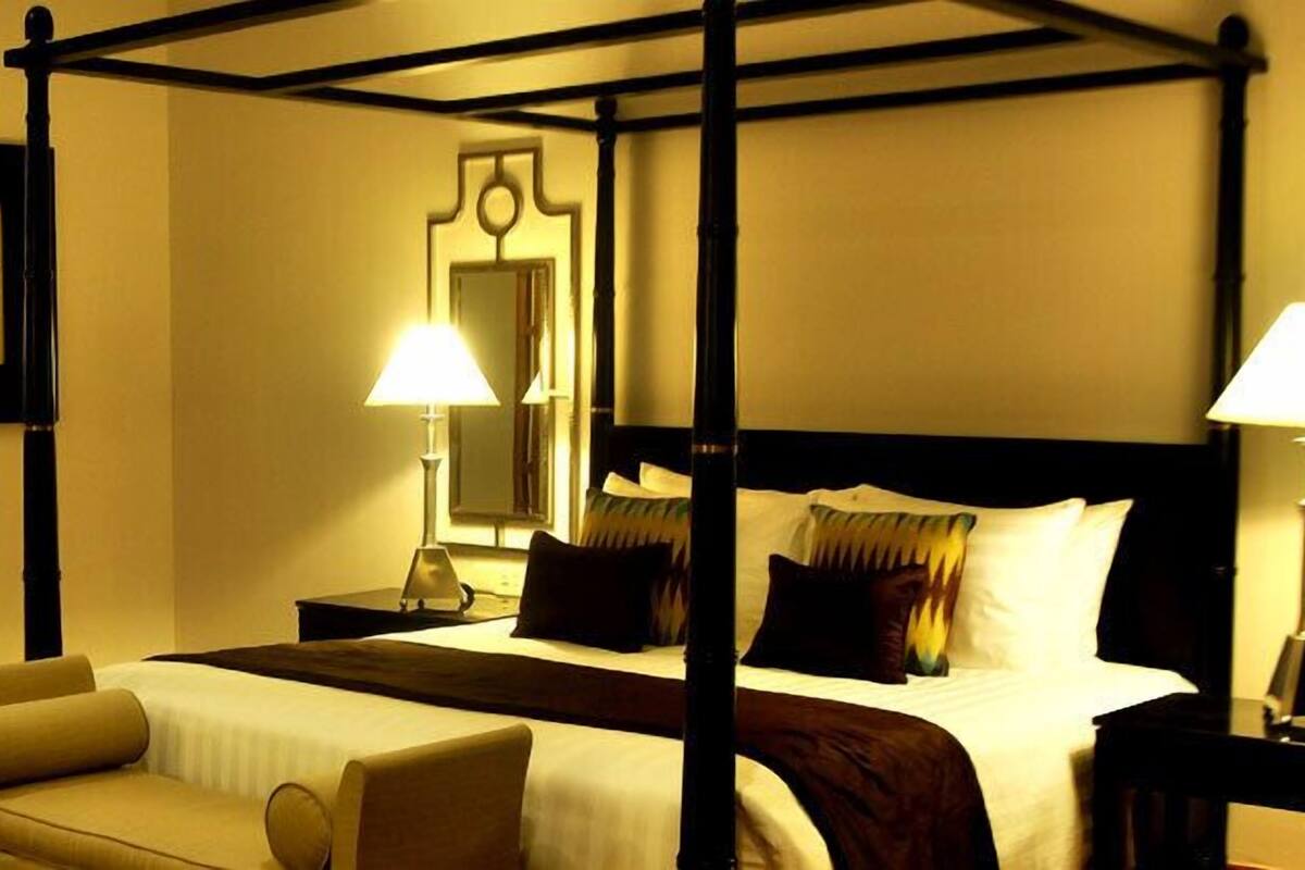 A four-poster bed with a nightstand, two bedside lamps, and a chair in a hotel room.