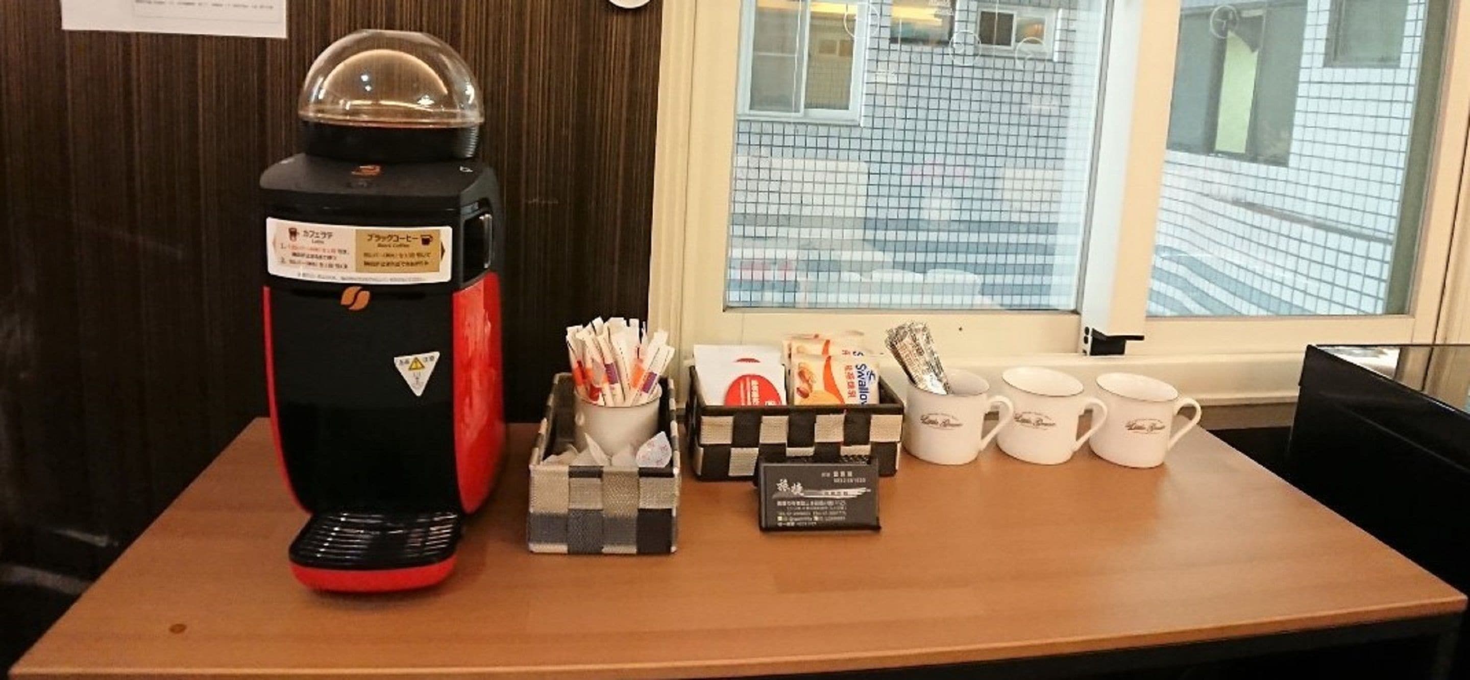 Una macchina da caffè, una confezione di capsule, una tazza di caffè e diverse mug su un tavolo.