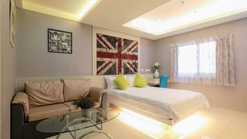 A modern hotel room with a bed, a sofa, a glass coffee table, and a wall with a Union Jack flag.