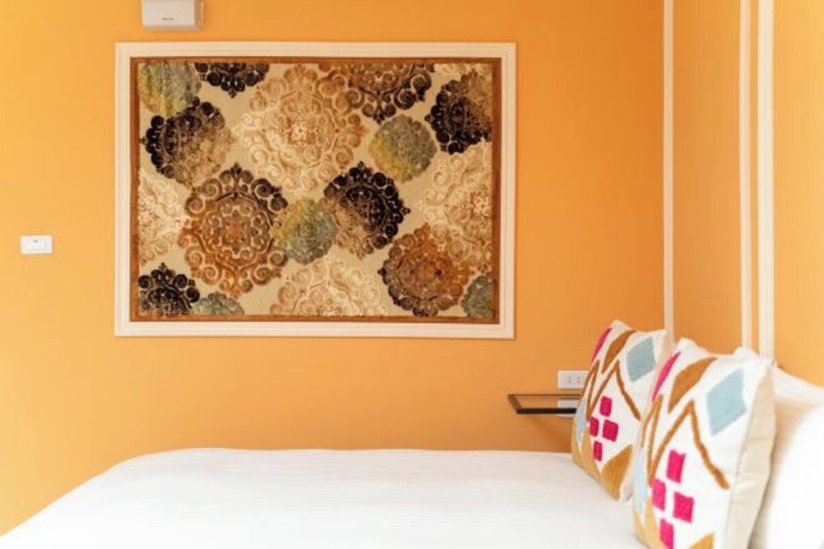 A bedroom with a bed, pillows, and a framed artwork on the wall.