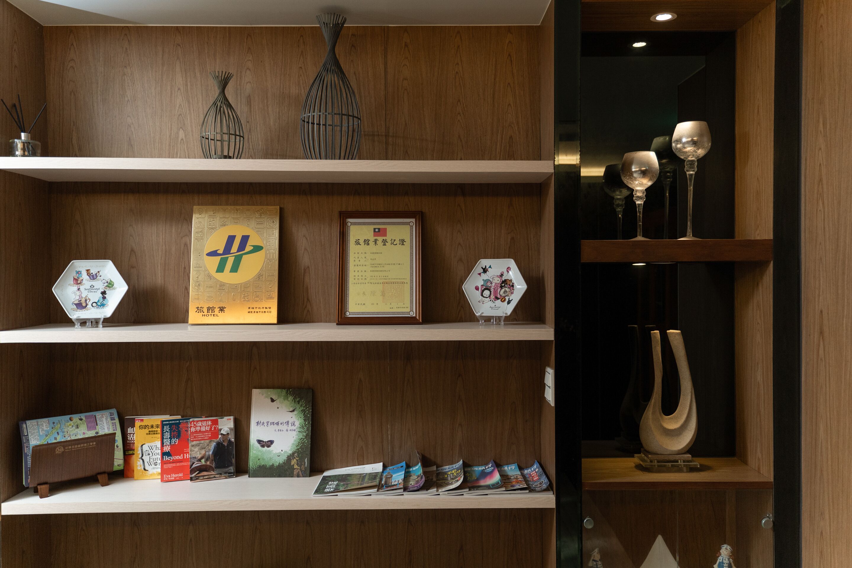 A wooden shelf with various items including books, framed certificates, and decorative objects.