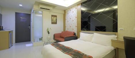 A hotel room with a bed, a desk, a chair, a sofa, and a small table with a vase.