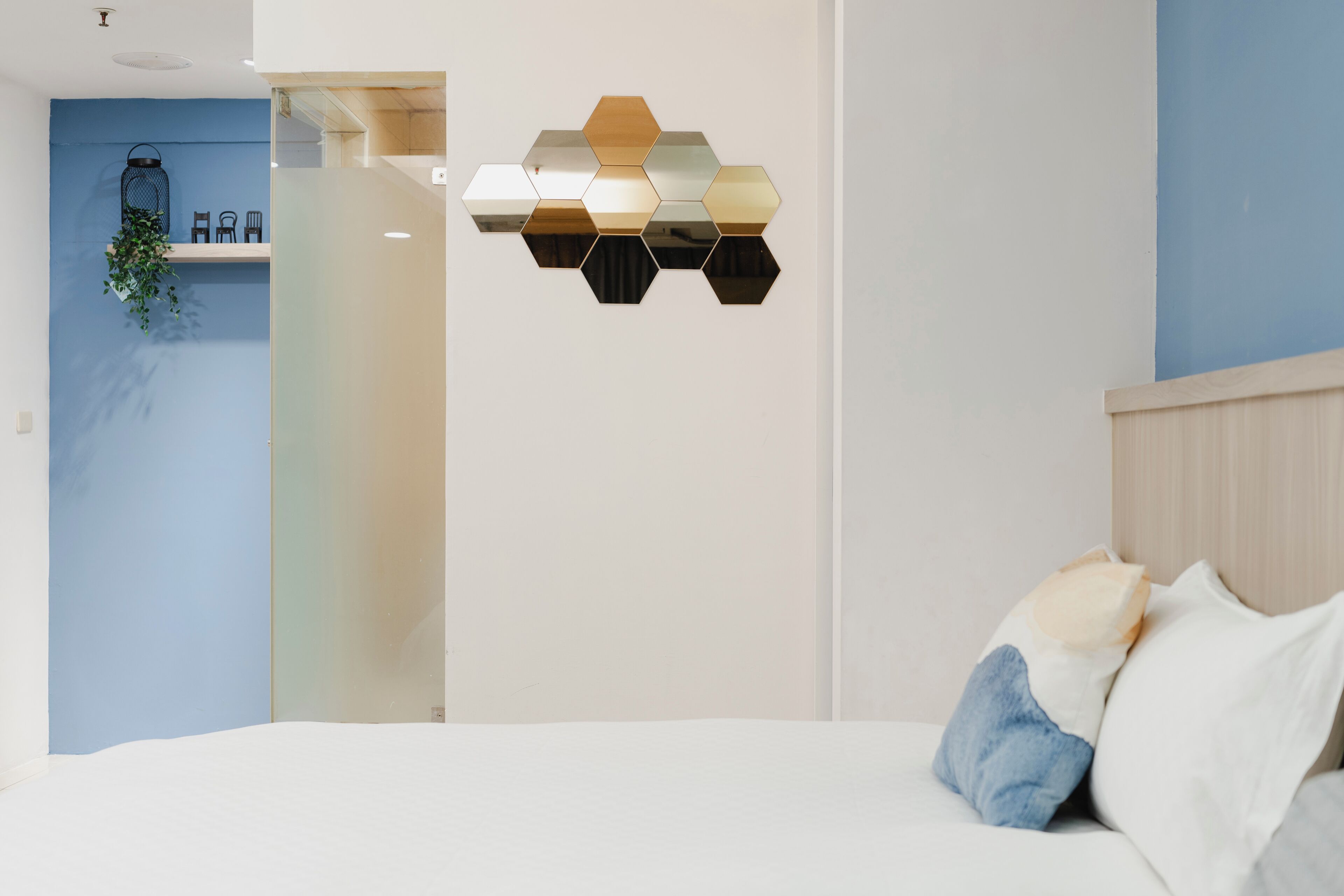 Un dormitorio moderno con cama, un espejo hexagonal montado en la pared y una pared de acento azul.