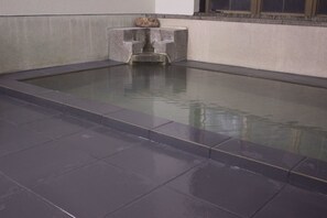Une piscine rectangulaire bordée de pierres, avec une petite structure en pierre au centre.