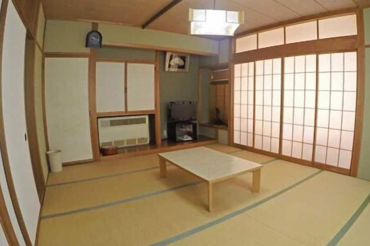 Une pièce de style japonais traditionnel, avec un sol recouvert de tatamis, une petite table en bois, des portes coulissantes en papier de riz (shoji) et un petit téléviseur.