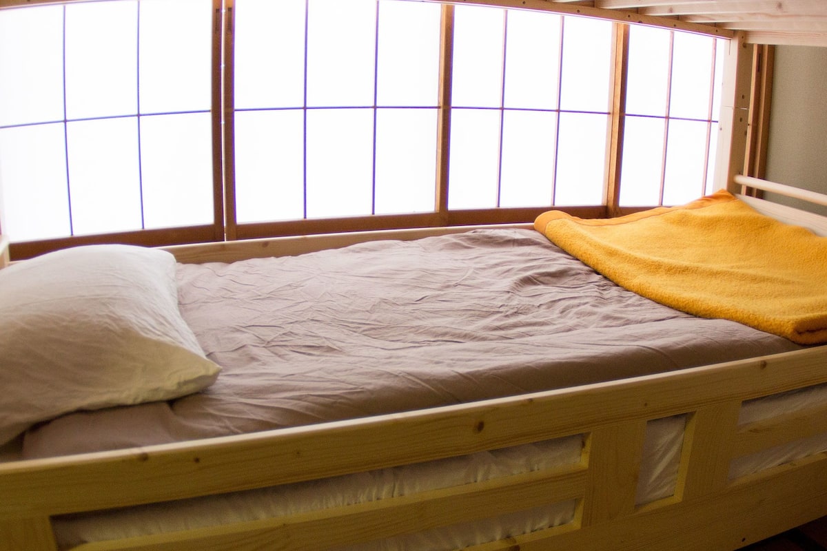 Un lit simple avec un cadre en bois, un oreiller blanc et une couverture jaune.