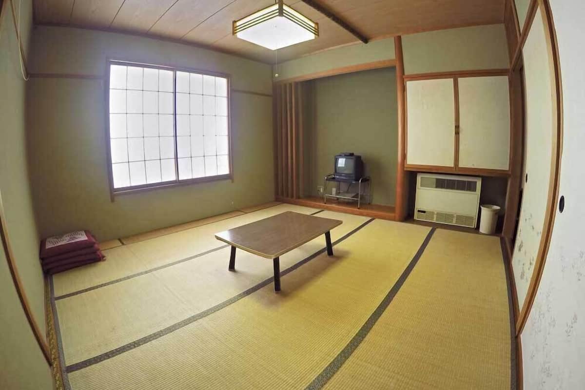 Une pièce de style japonais traditionnel, avec un sol recouvert de tatamis, une table basse, un téléviseur et des portes coulissantes.