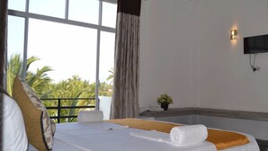 A hotel room with a bed, a window with curtains, a small table with a plant, and a wall-mounted TV. - Leighton Resort (Negombo)