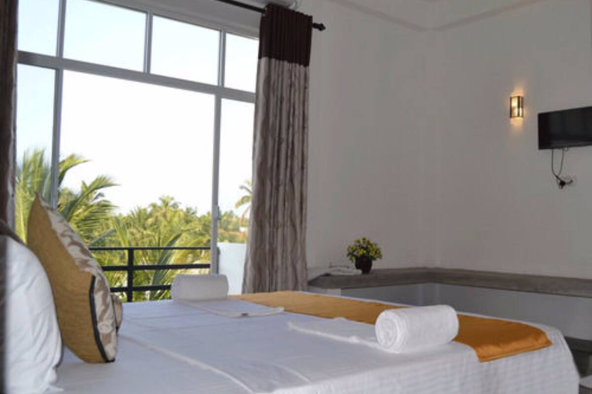 A hotel room with a bed, a window with curtains, a small table with a plant, and a wall-mounted TV.