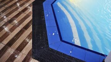 A pool area with a wooden deck and a blue tiled section.