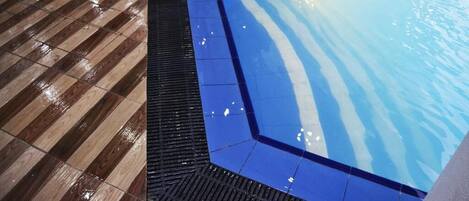 A pool area with a wooden deck and a blue tiled section.
