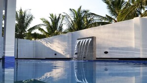 A pool with a waterfall feature, surrounded by a white wall and palm trees. - Leighton Resort (Negombo)
