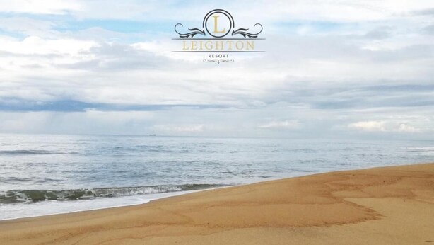 A beach with footprints leading to the water, and the Leighton Resort logo in the sky. - Leighton Resort (Negombo)