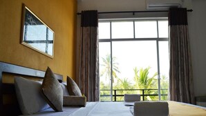 A hotel room with a large window, a bed with pillows, a bedside table, and a framed picture on the wall. - Leighton Resort (Negombo)