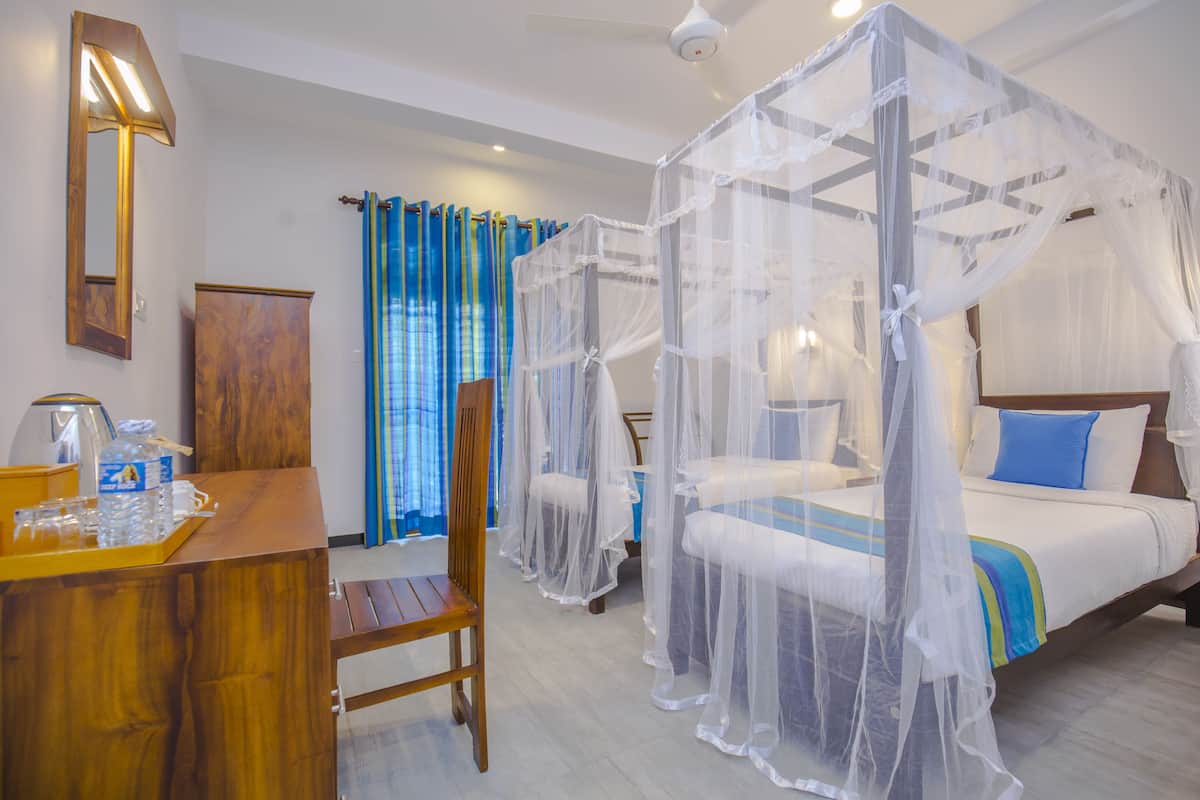 A hotel room with a wooden desk, a chair, a bed with a canopy, and a window with blue curtains.