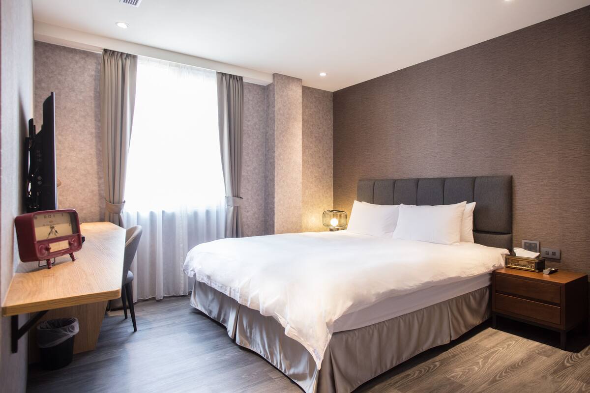 Une chambre d’hôtel moderne avec un grand lit, une table de chevet et un bureau avec une chaise.