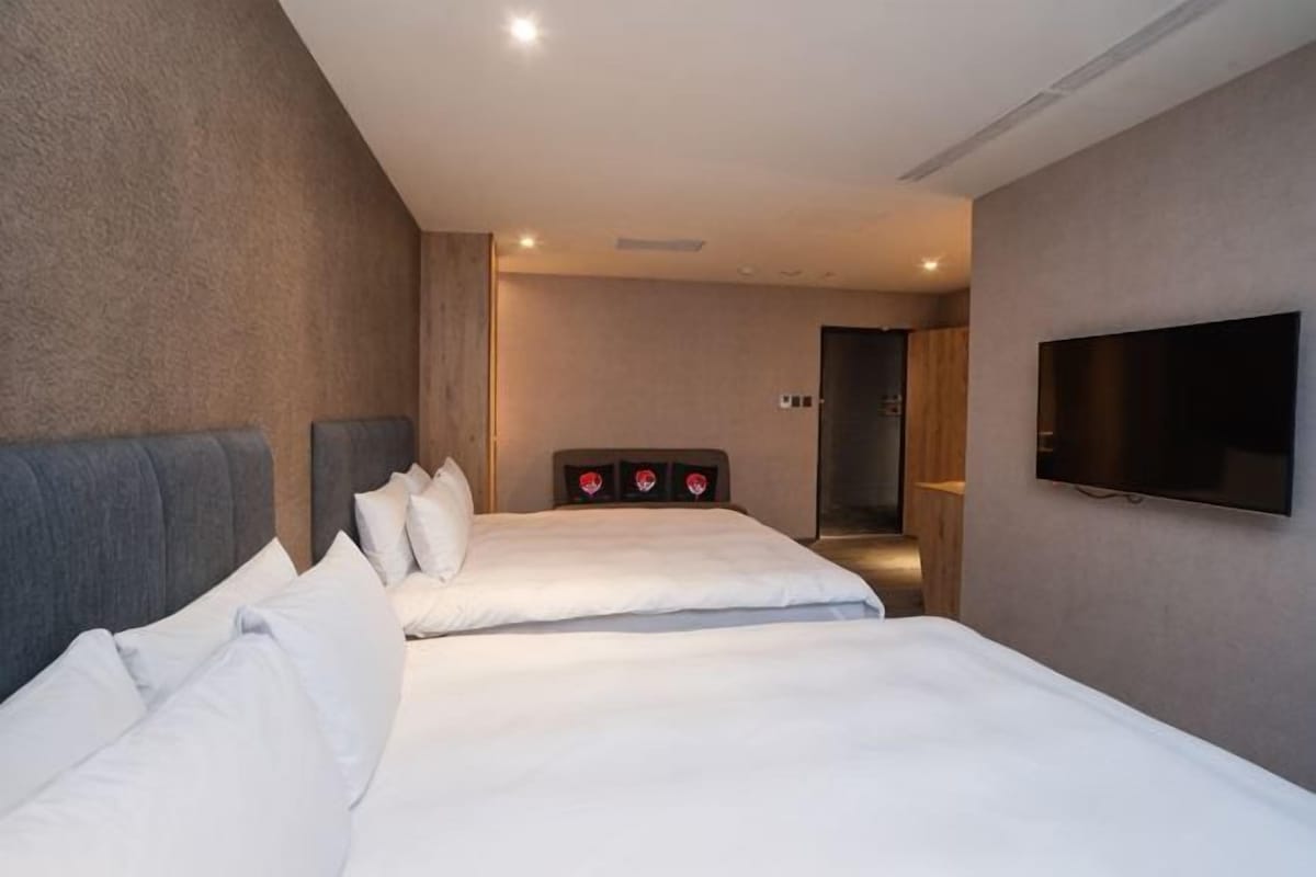 A hotel room with two beds, a flat-screen TV, and a bathroom visible through an open door.