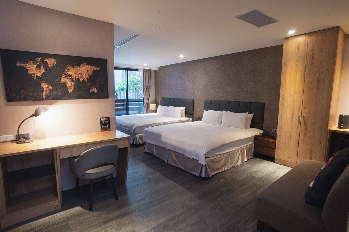 Une chambre d’hôtel avec deux lits, un bureau, une chaise, une armoire et une carte du monde accrochée au mur.