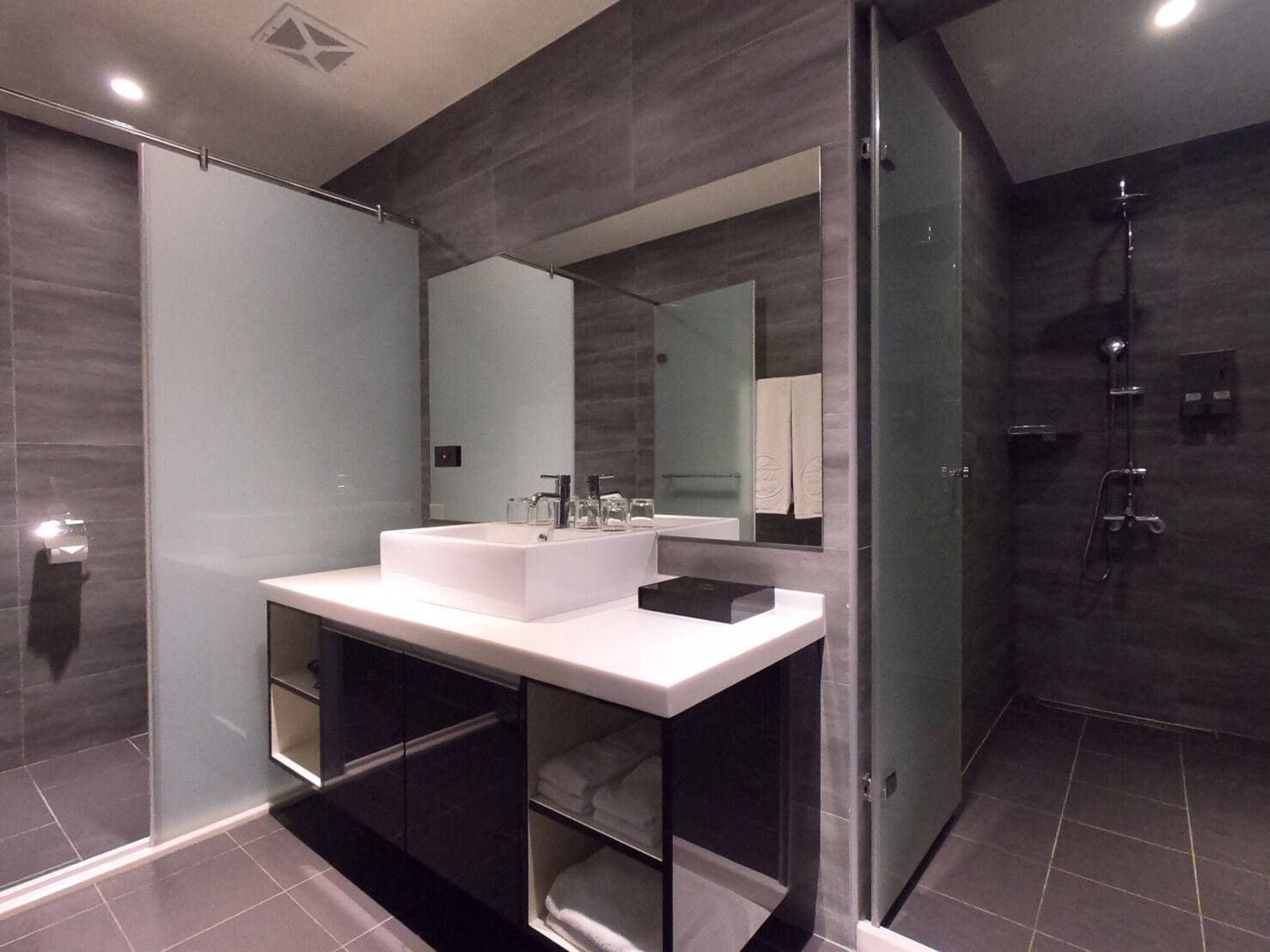 A modern bathroom with a large mirror, a white sink, and a glass-enclosed shower area.
