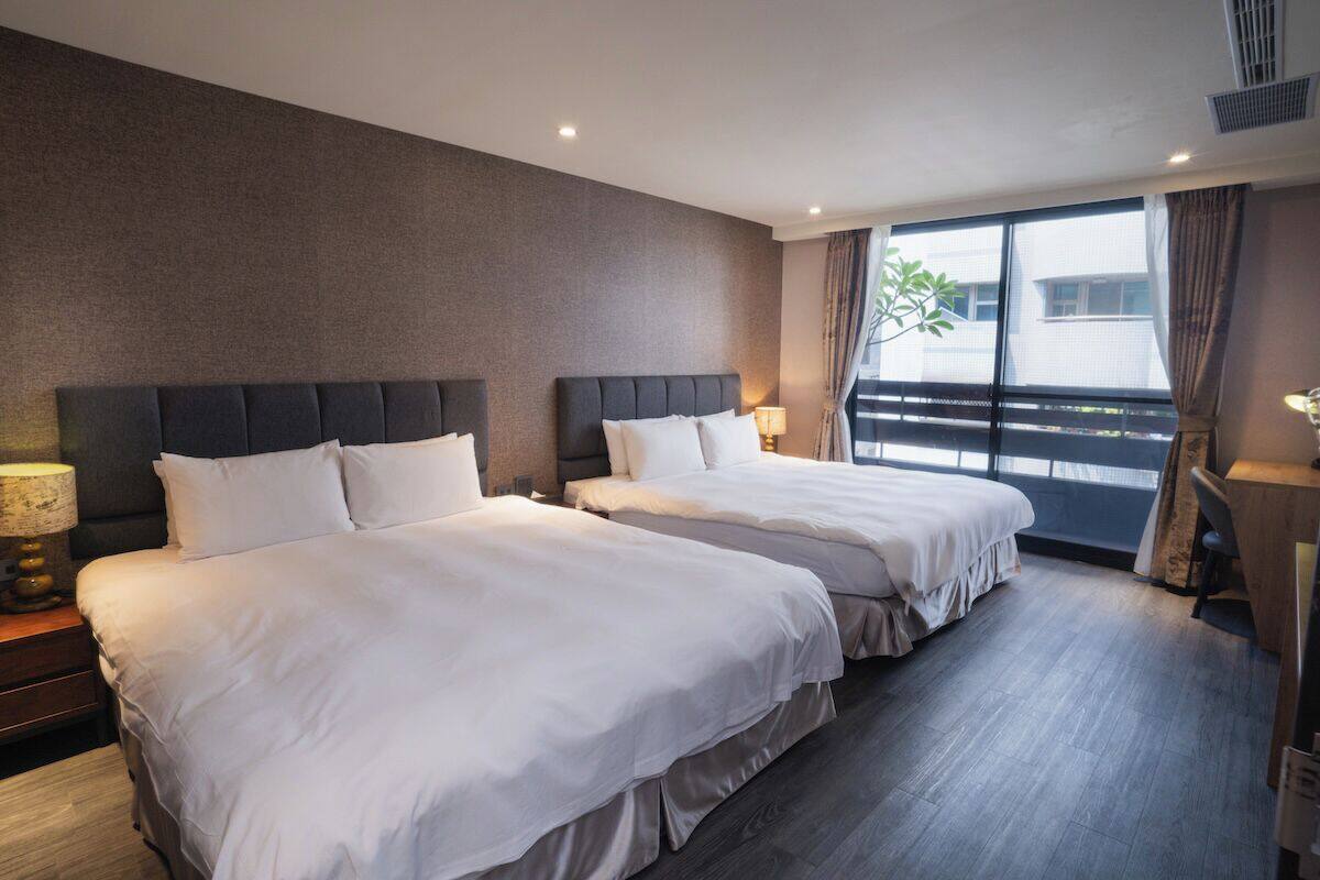Une chambre d’hôtel avec deux lits, une grande fenêtre avec des rideaux, un bureau et une chaise.
