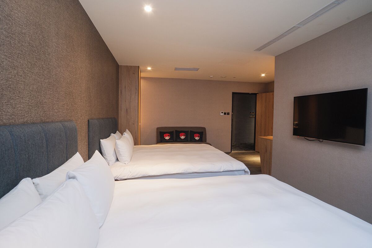 Habitación de hotel con dos camas, un televisor de pantalla plana y un cabecero de madera.