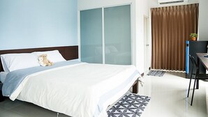 A hotel room with a bed, a desk, a chair, a wardrobe, and an air conditioning unit. - Yada Living (Surat Thani)