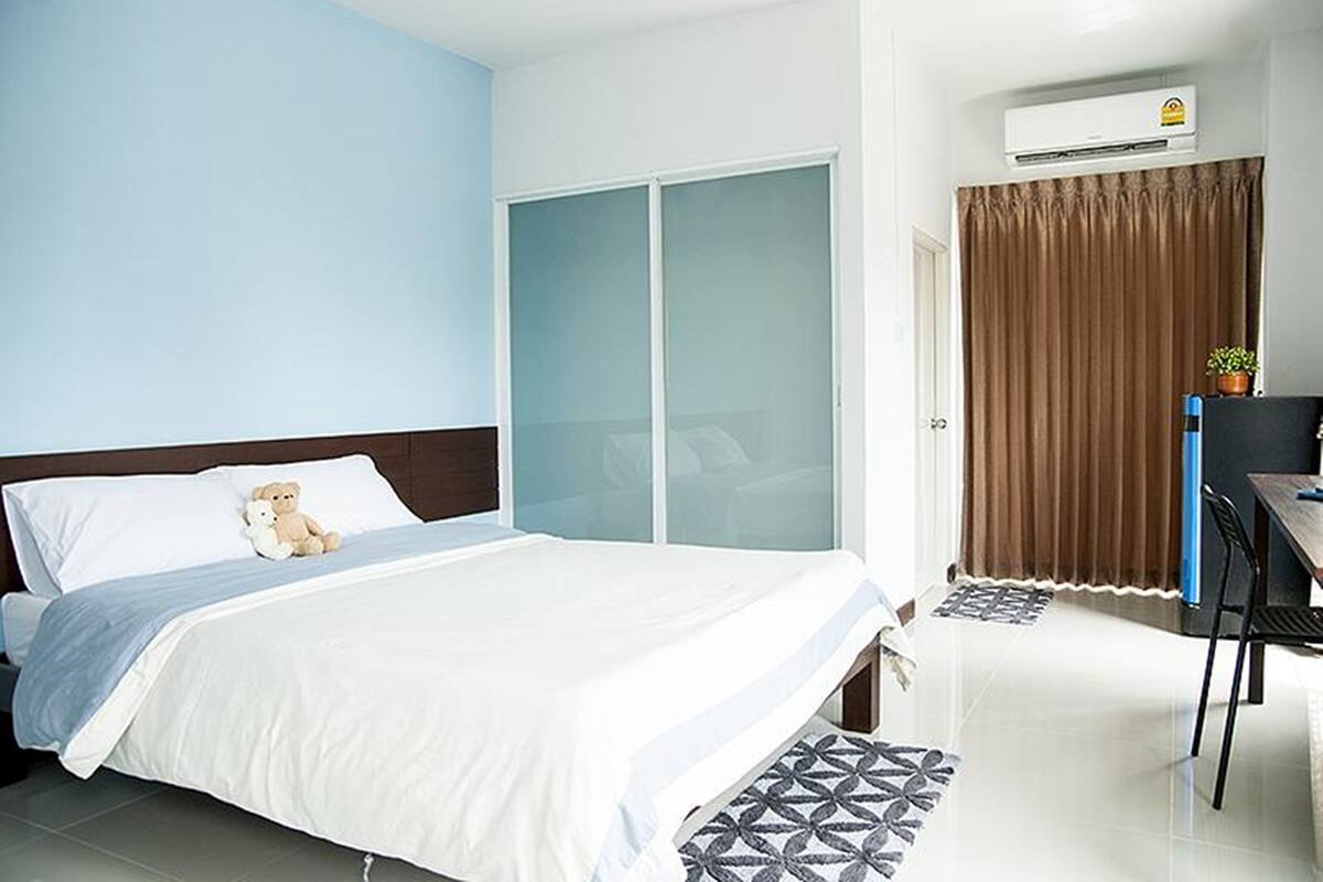 A hotel room with a bed, a desk, a chair, a wardrobe, and an air conditioning unit.