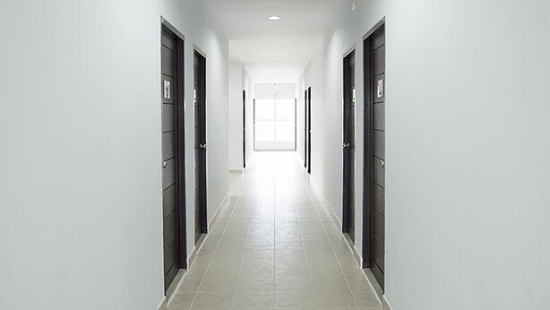 A long, narrow hallway with dark doors on both sides and a tiled floor. - Yada Living (Surat Thani)