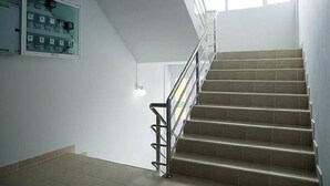 A staircase with a metal handrail, a wall-mounted electrical panel, and a window providing natural light. - Yada Living (Surat Thani)