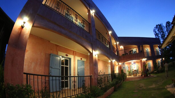 A multi-story hotel with balconies, a well-lit entrance, and a landscaped garden. - Le Bar Tarry Hotel (Tha Li)