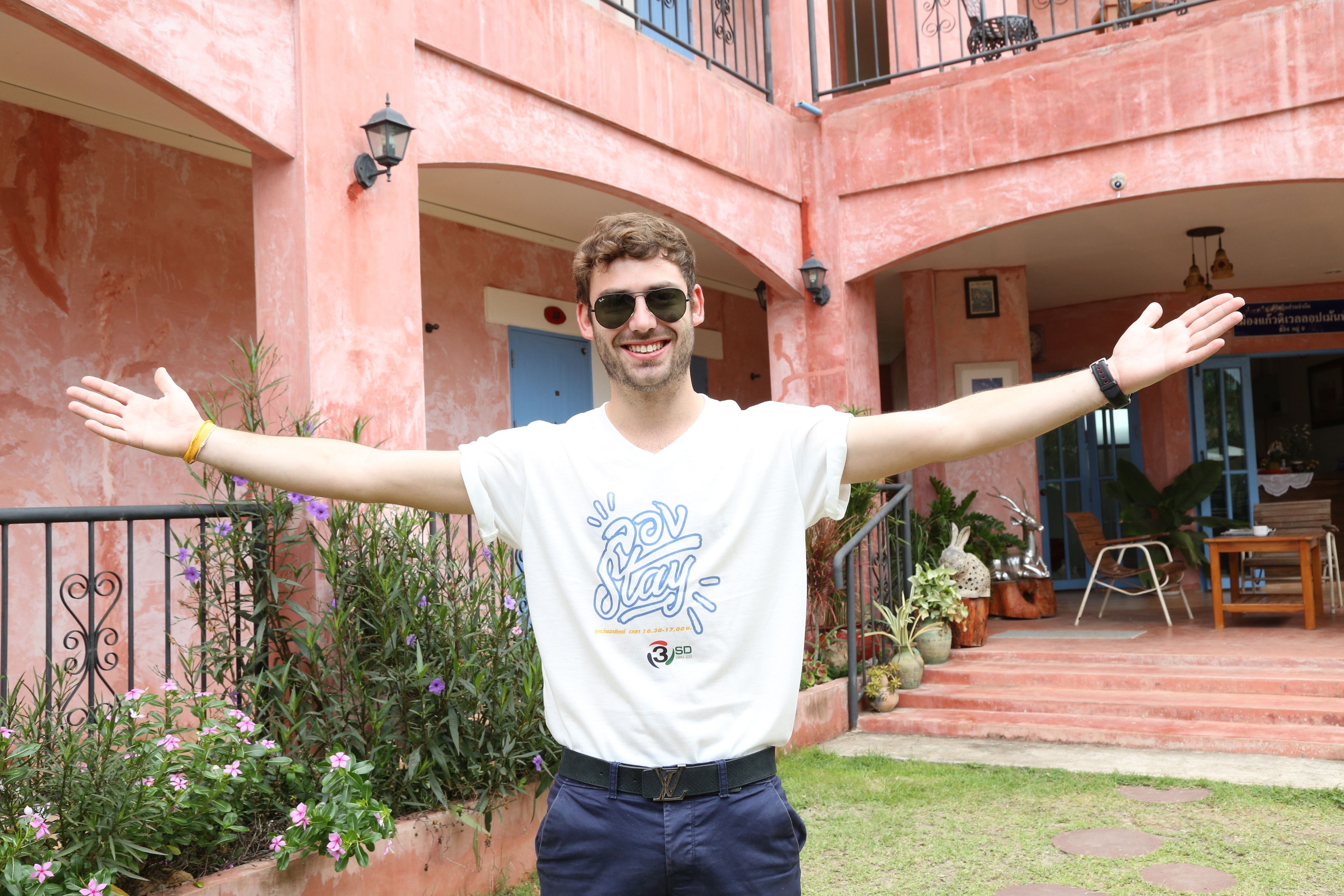 A person standing in front of a building with arches and potted plants.